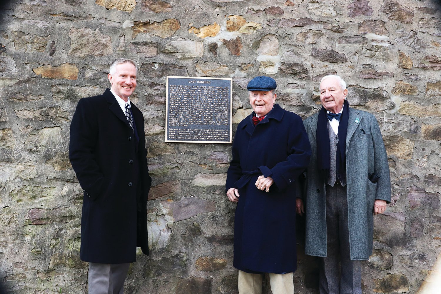 Charles Meredith, center, Larry Grim, right, and his son Gregory Grimm, left, stand by a new plaque on the walls of the old Bucks County Prison. The title is “Last Hanging.” It tells the tale of Charles Meredith’s grandfather, the Bucks County sheriff (who was in charge of the execution), and Larry Grim’s  great-uncle, who was the court appointed public defender for the convicted murderer. Photograph by Rebecca Rosen