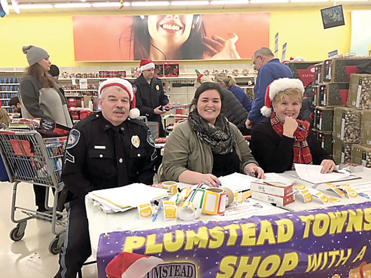 Plumstead Cpl. Michael Johnson, his daughter, Caitlin Johnson and Township Manager Carolyn McCreary welcome families to Plumstead’s Shop With a Cop event at Plumstead K Mart. Photograph by Rebecca Fink.