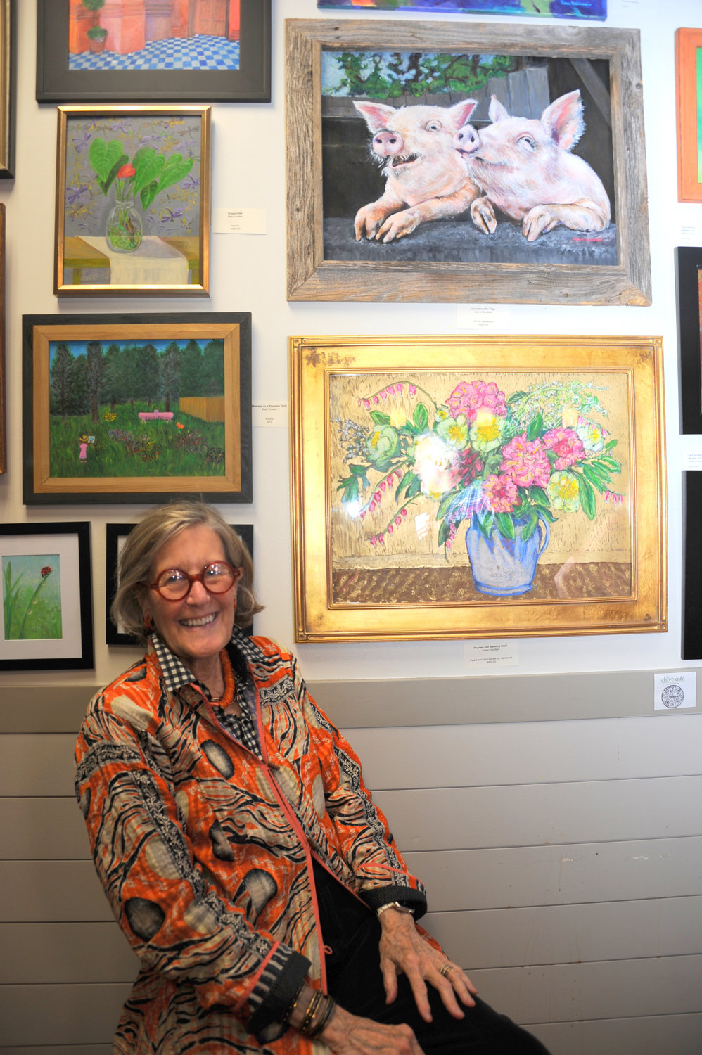 JoAnn Goodwin sits under her painting, “Lunchtime
for pigs.”