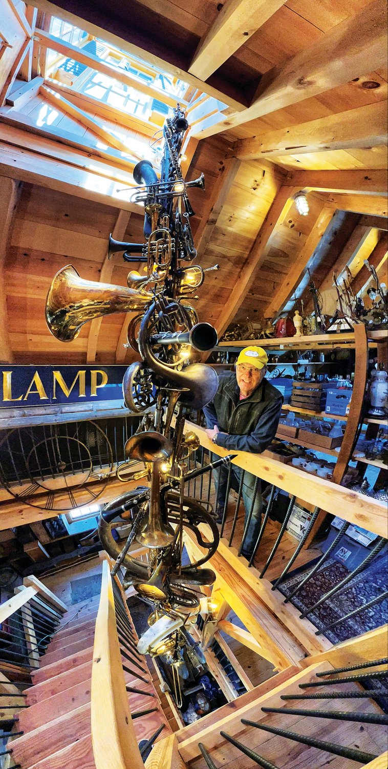 Doug Zegel, of Doylestown, stands beside his extraordinary 21-foot-long “chandelier” made entirely from wind instruments.