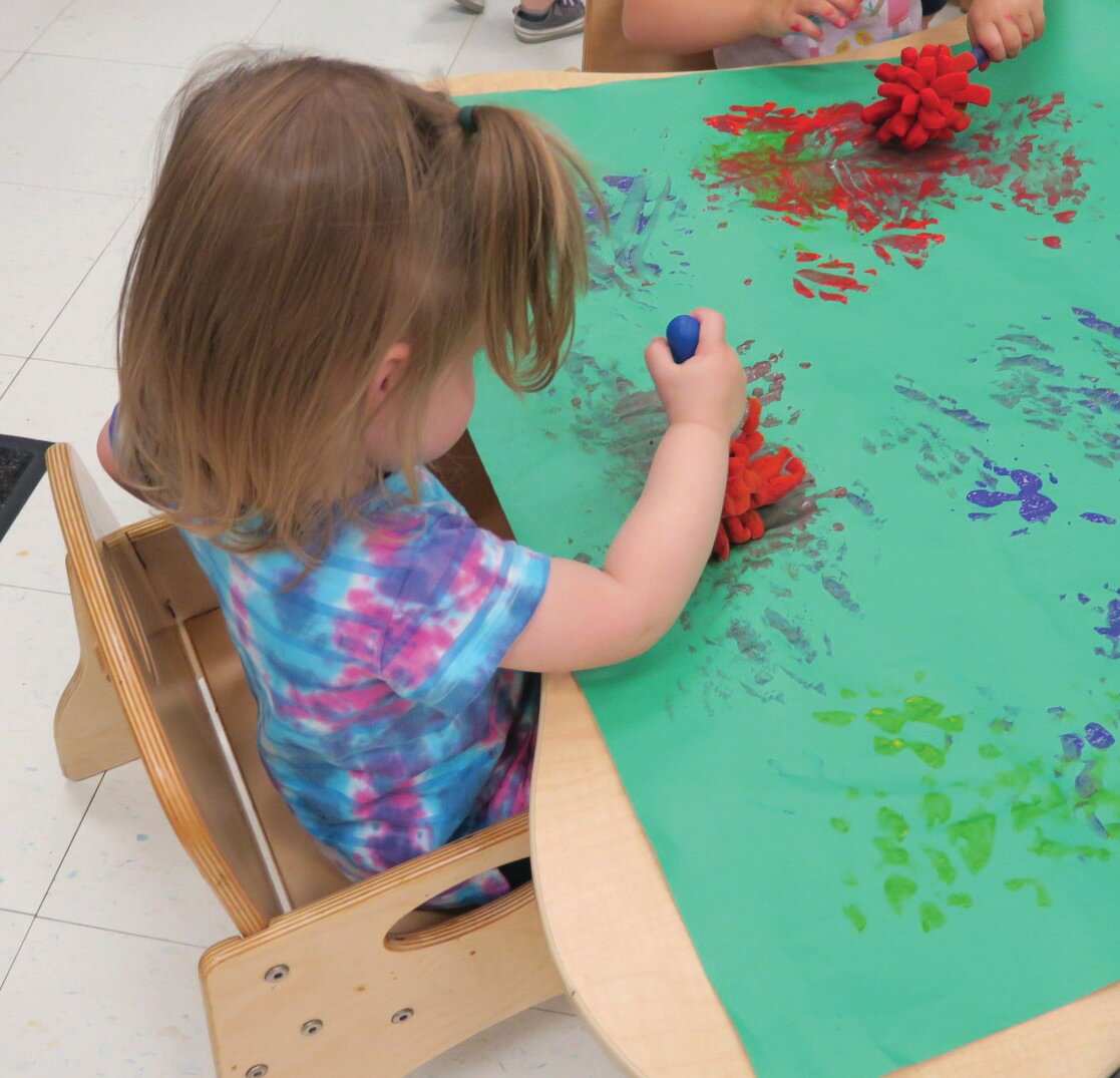 A 1-year-old explores painting with sponge wands at the YMCA Child Learning Center.